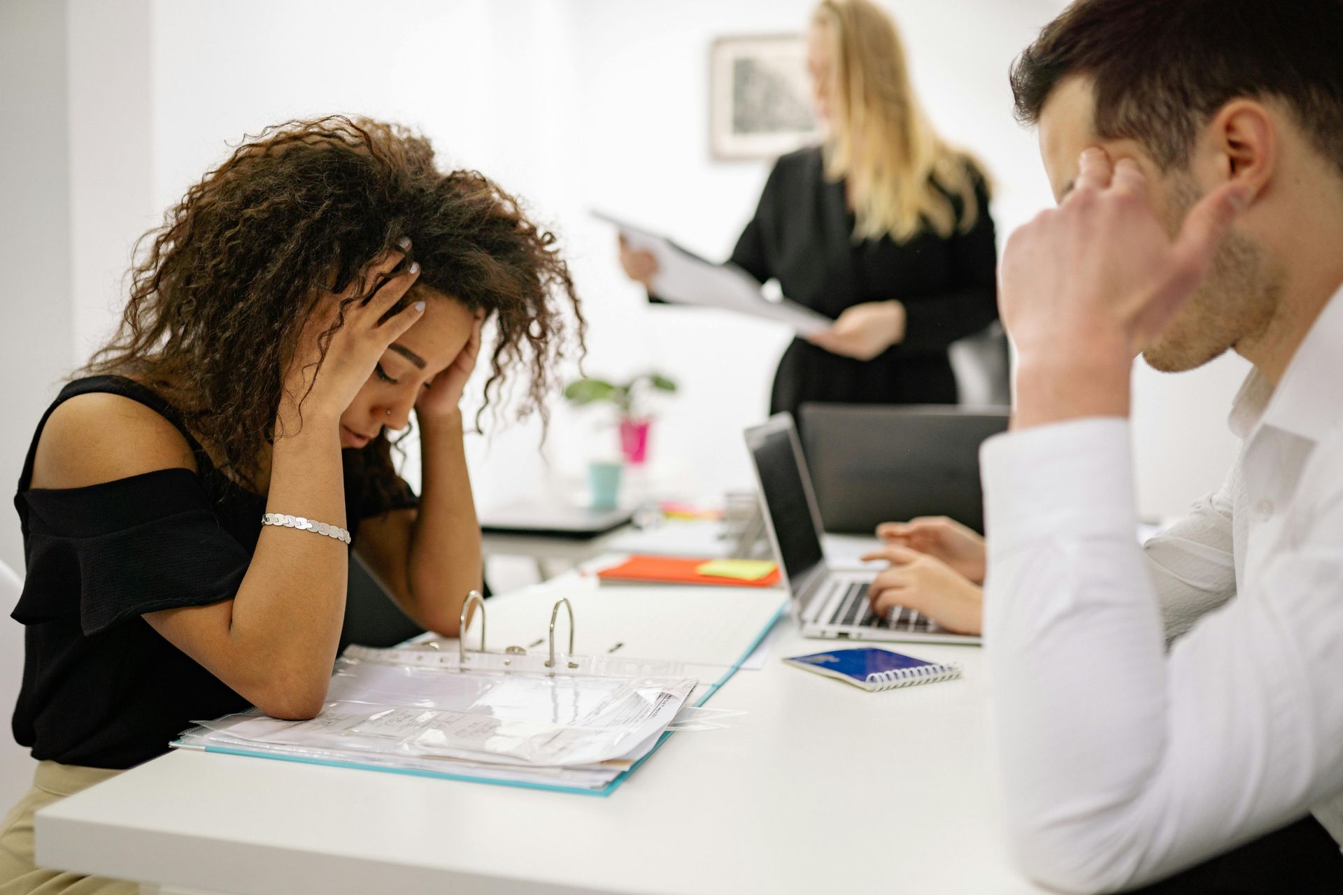 A woman holds her head in her hands, looking stressed at work.