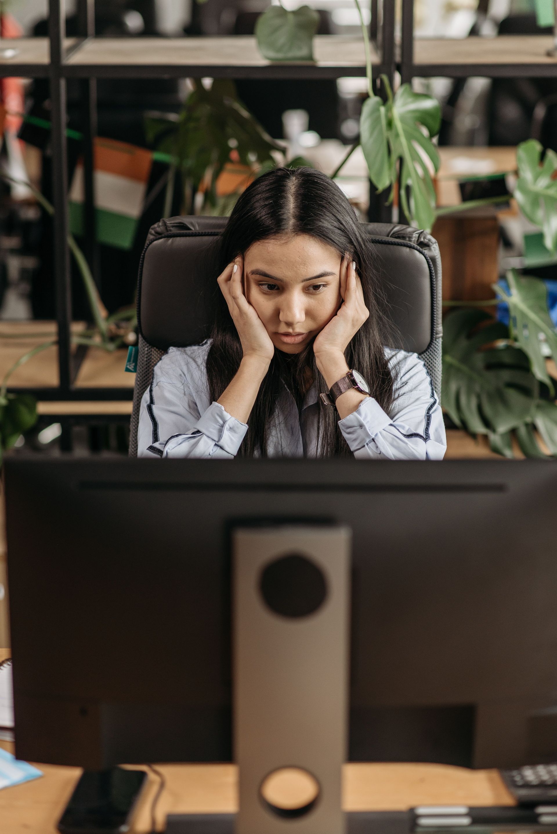 Woman at a desk, hands on her temples, looking stressed at a computer in an office.