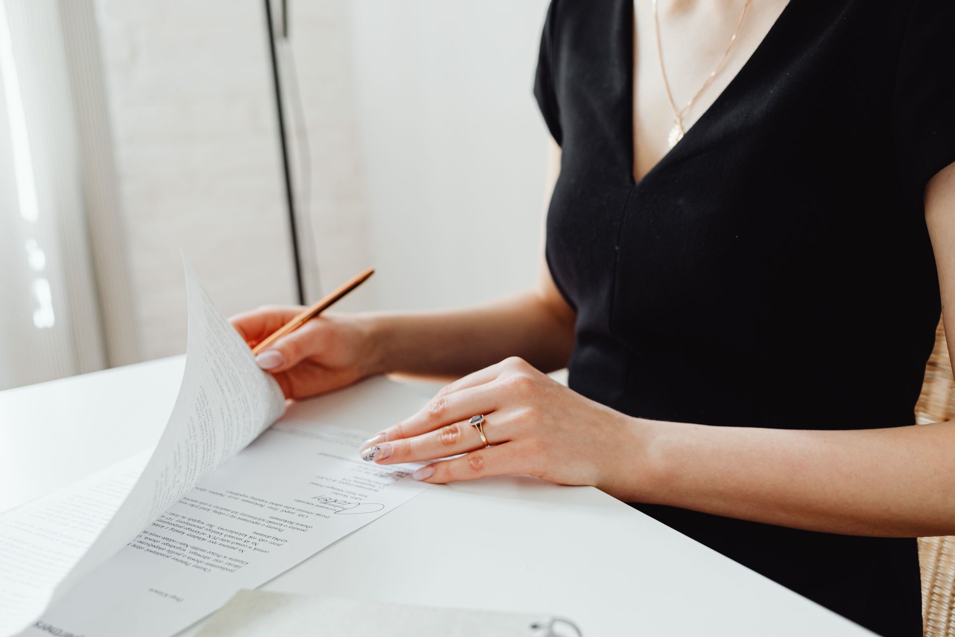 Person in black top writing on documents at a white desk with a pencil