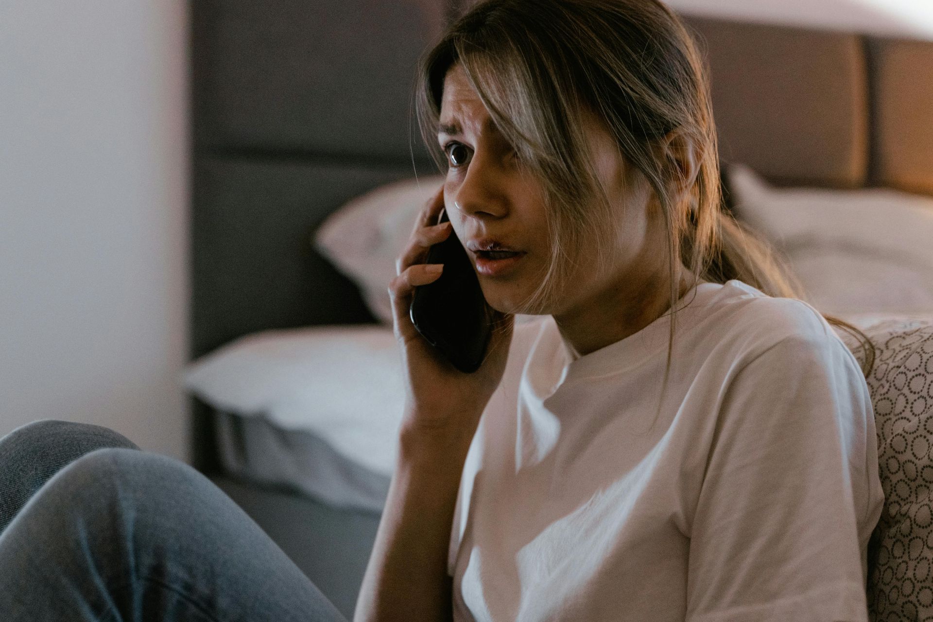 A scared woman is sitting on the floor talking on a cell phone.