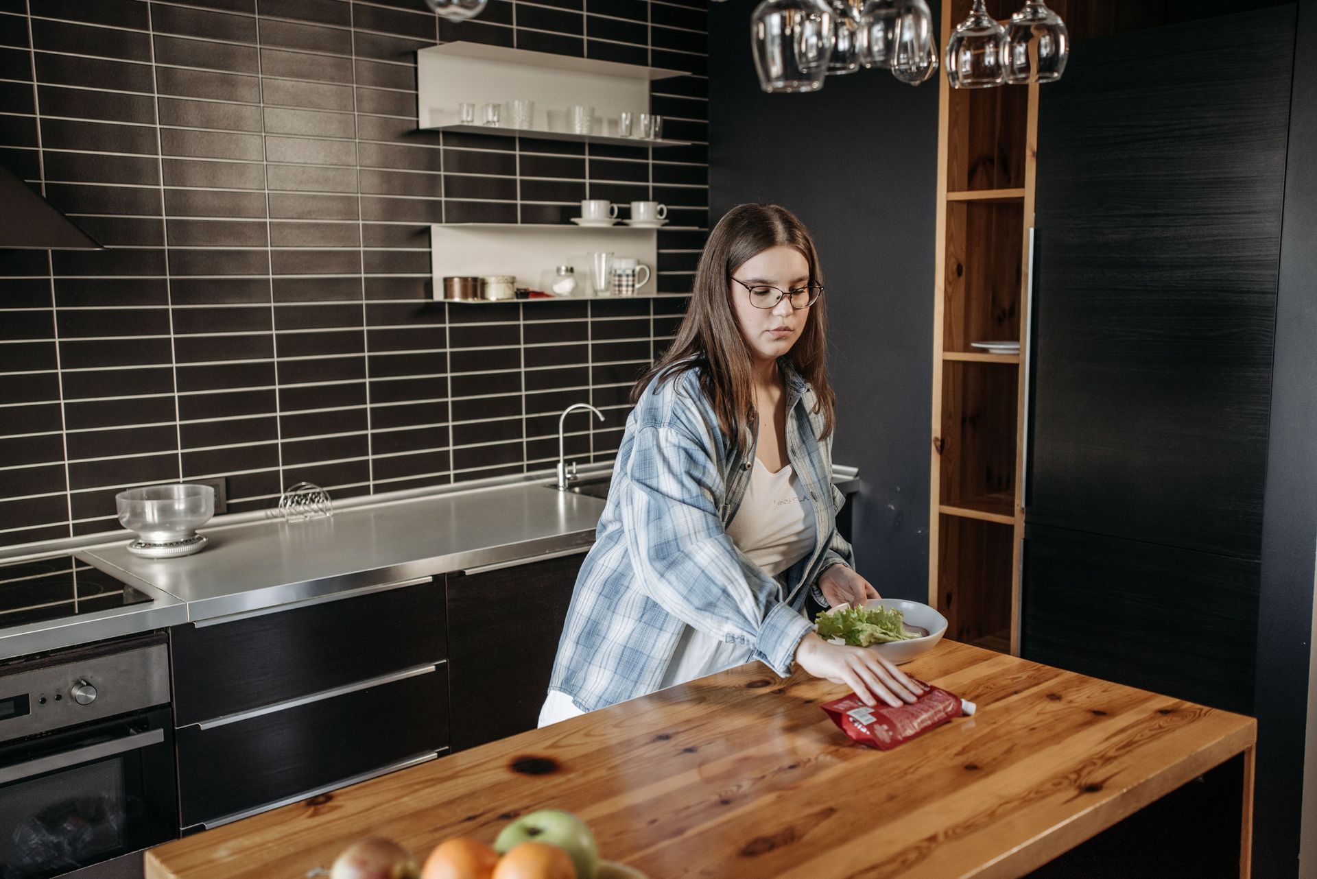 Girl chopping vegetables at a wooden kitchen island in a modern black-tiled kitchen