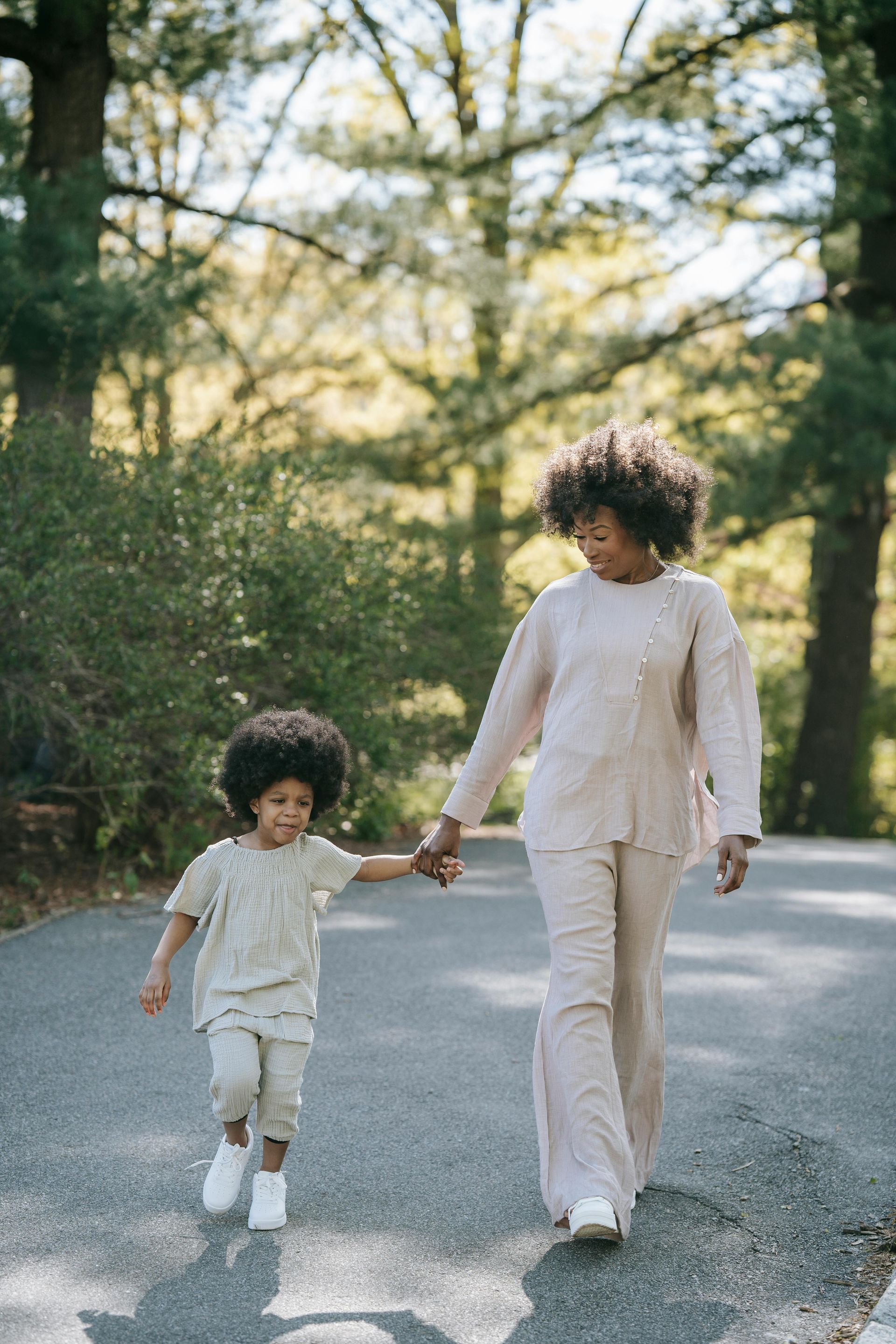Two people walking hand in hand on a tree-lined road in soft sunlight