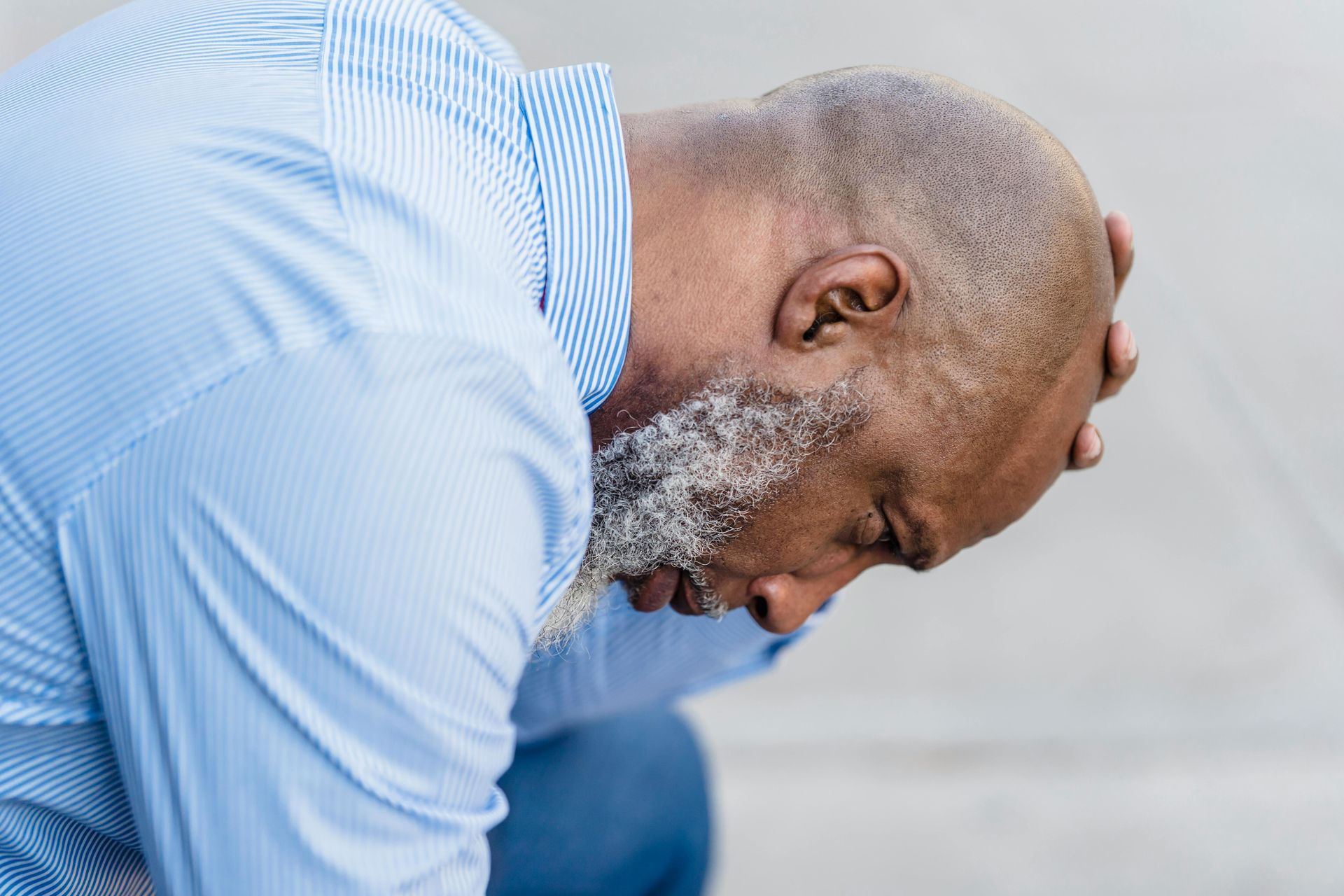 Man in a light blue shirt leaning forward with head bowed, looking distressed or tired