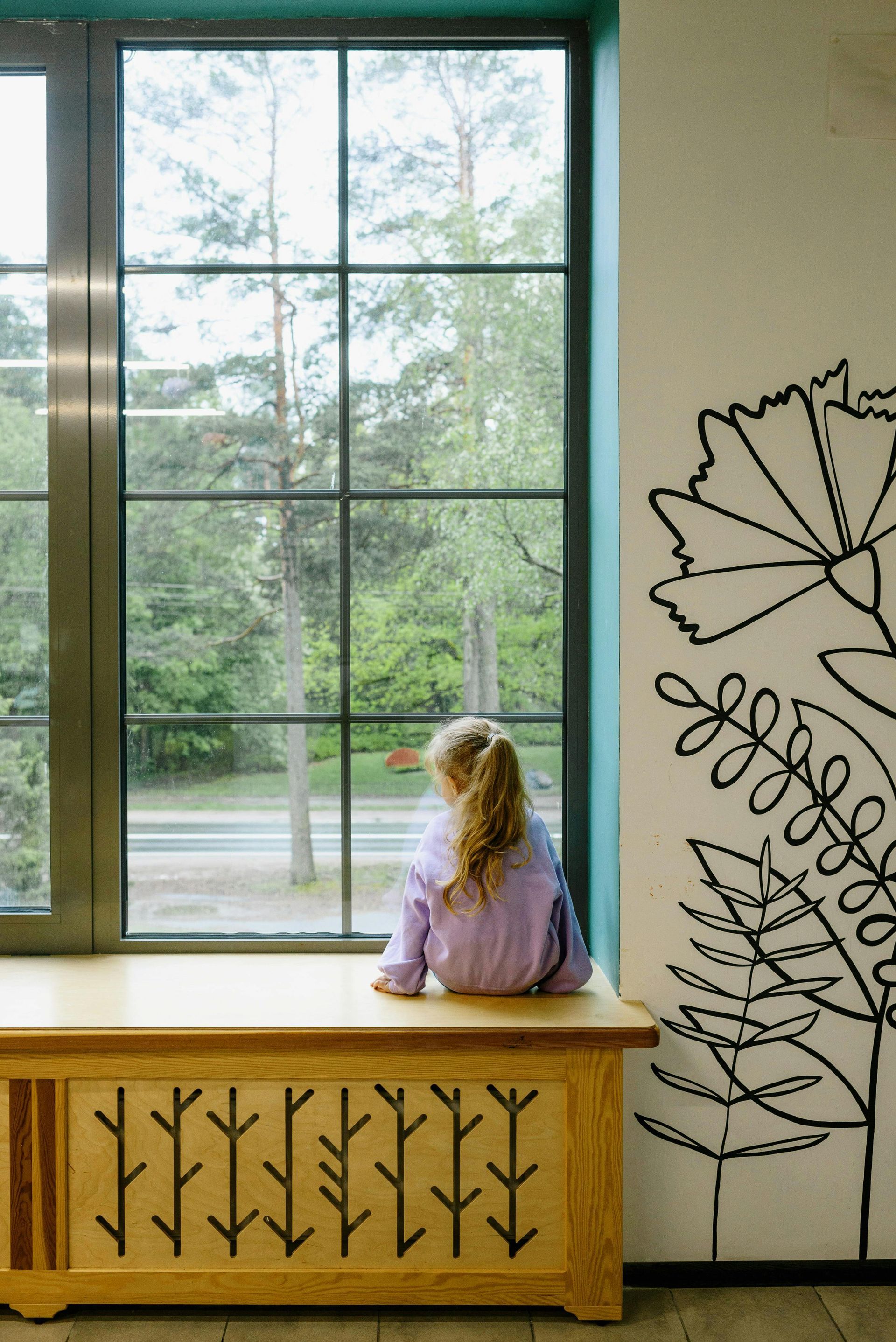 A little girl is sitting on a bench looking out a window.