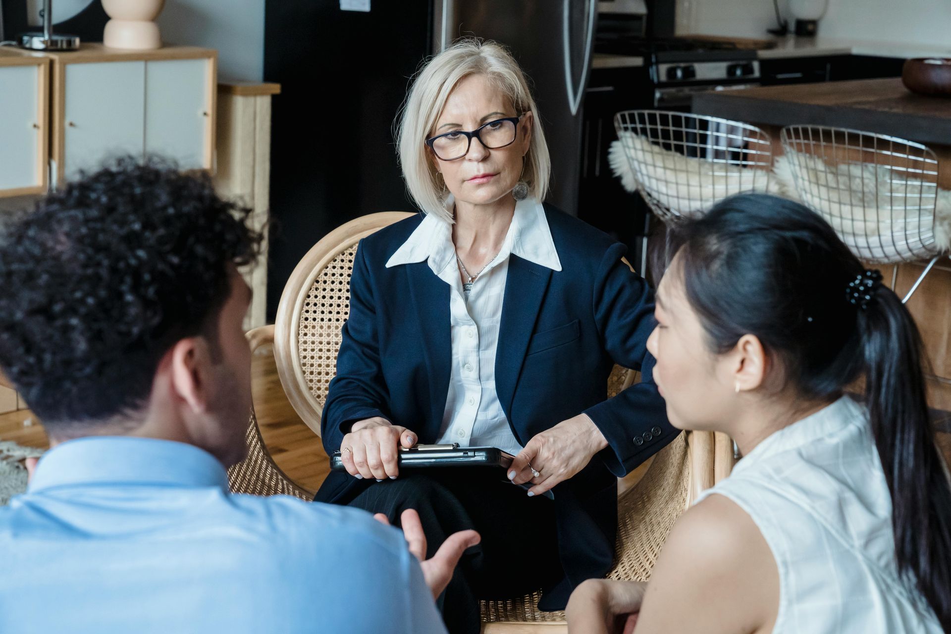 Counselor meeting with two seated clients in a office, one holding a tablet.