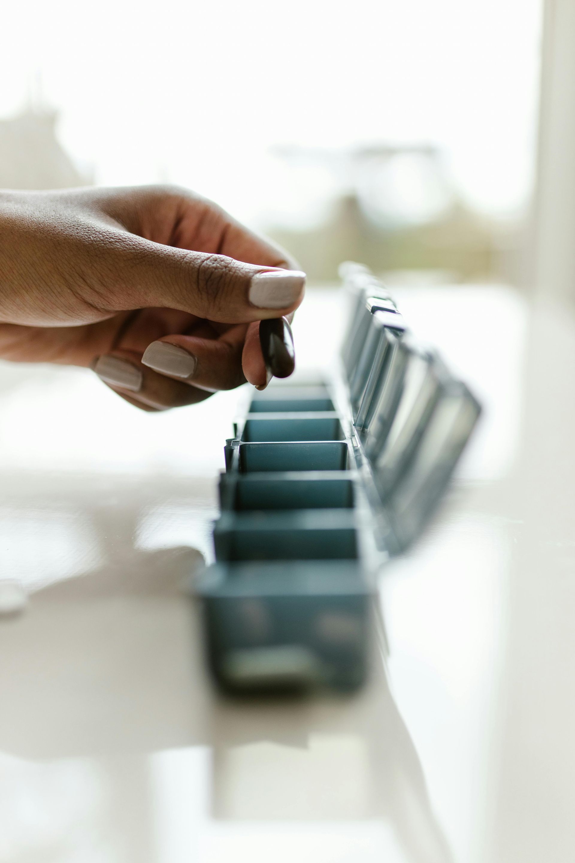 Hand placing a dark pill into a section of a pill organizer.