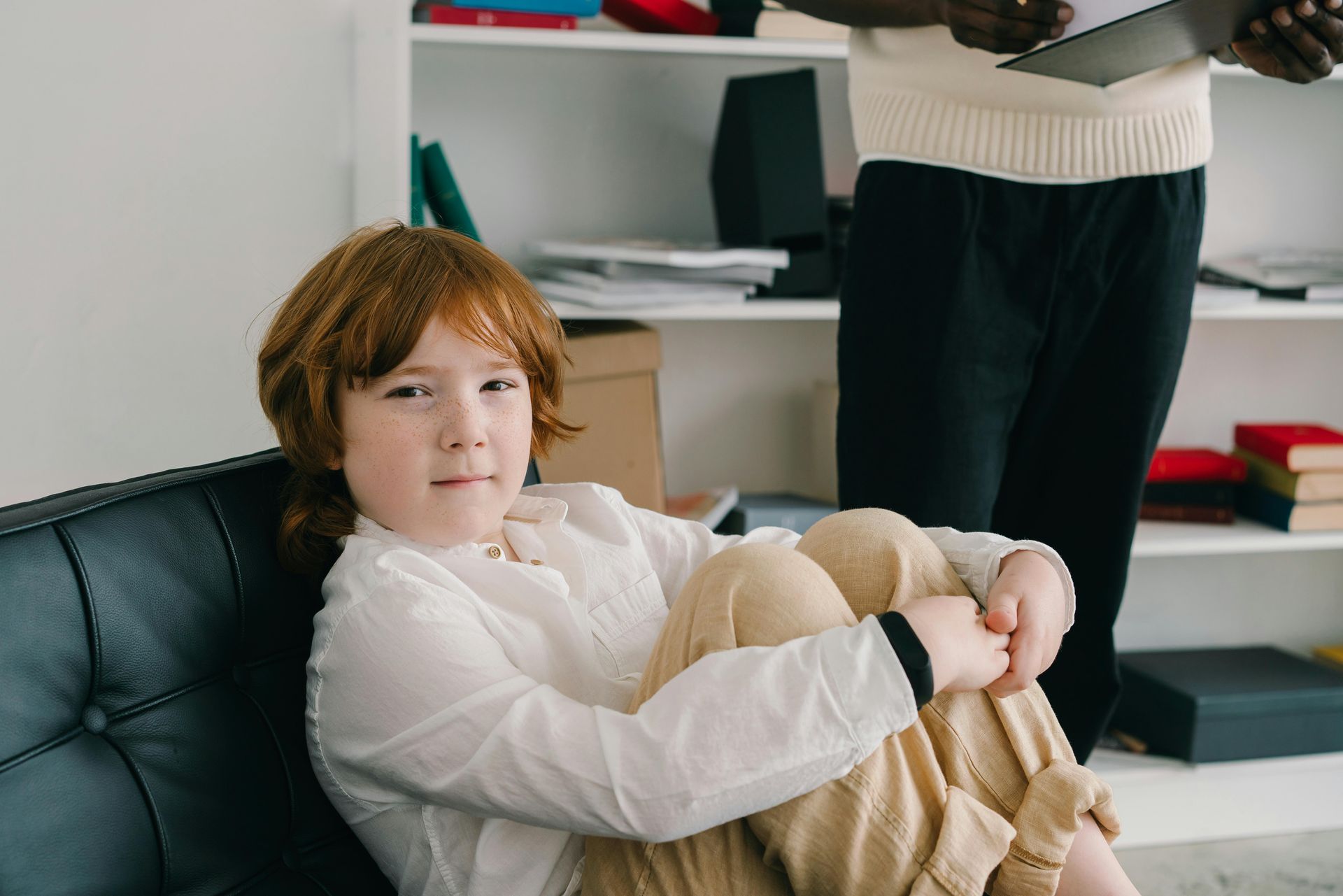 A child is sitting on a couch with thher legs crossed.