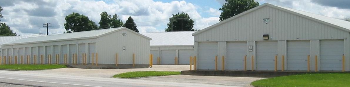 White storage buildings with gray doors under a cloudy sky.