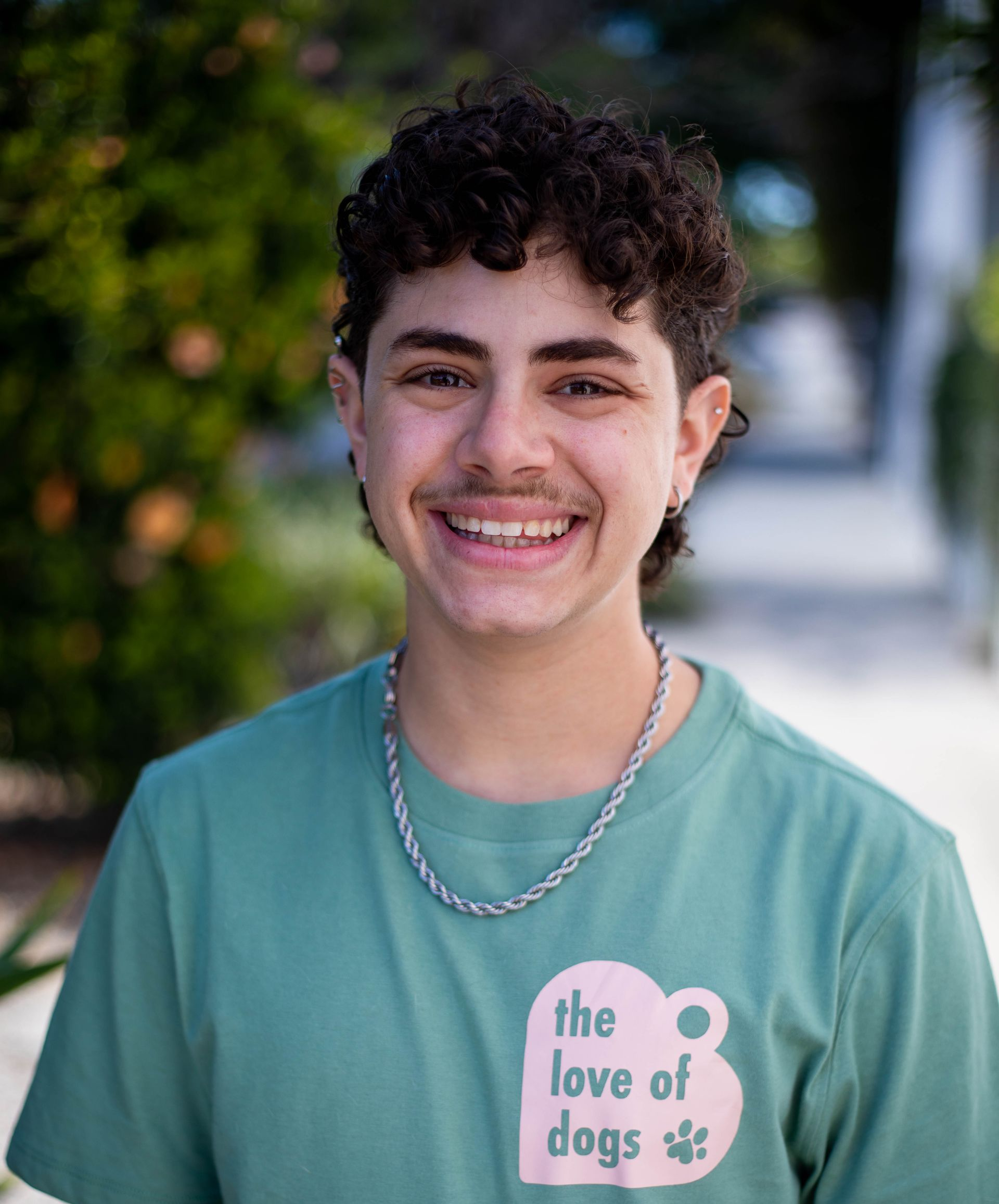 Person with curly hair and glasses smiles broadly, wearing a green polo shirt.