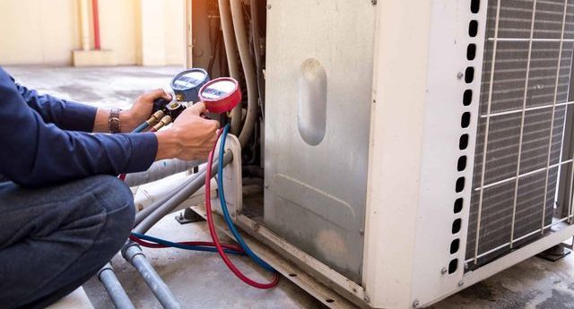 Technician cleaning a wall-mounted air conditioner with a vacuum hose in a workshop.
