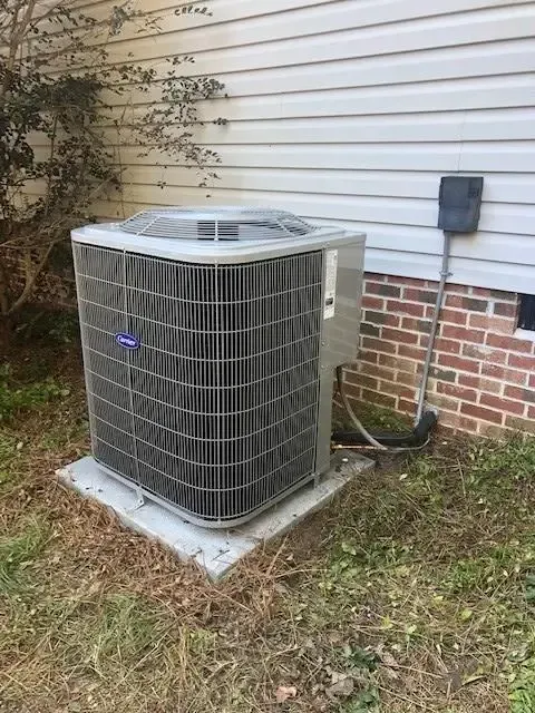 Outdoor air conditioning unit beside a house with white siding and a brick foundation