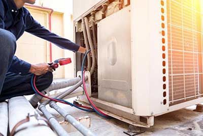 Technician checking outdoor HVAC unit with red gauge hose and tools near exposed pipes