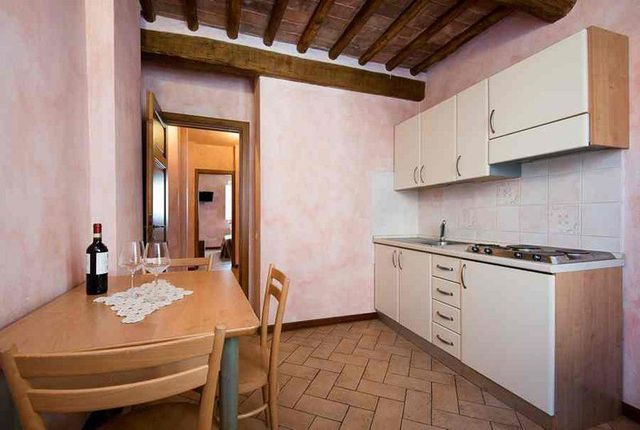 Piccola cucina con tavolo in legno, mobili bianchi, pavimento piastrellato e soffitto con travi a vista.