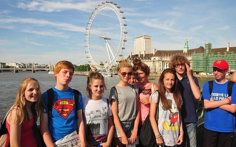 Group of teens posing with the London Eye in the background, sunny day.