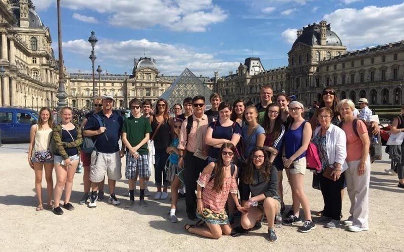 Group of tourists in front of the Louvre Museum in Paris, France; sunny day, various ages, smiling.