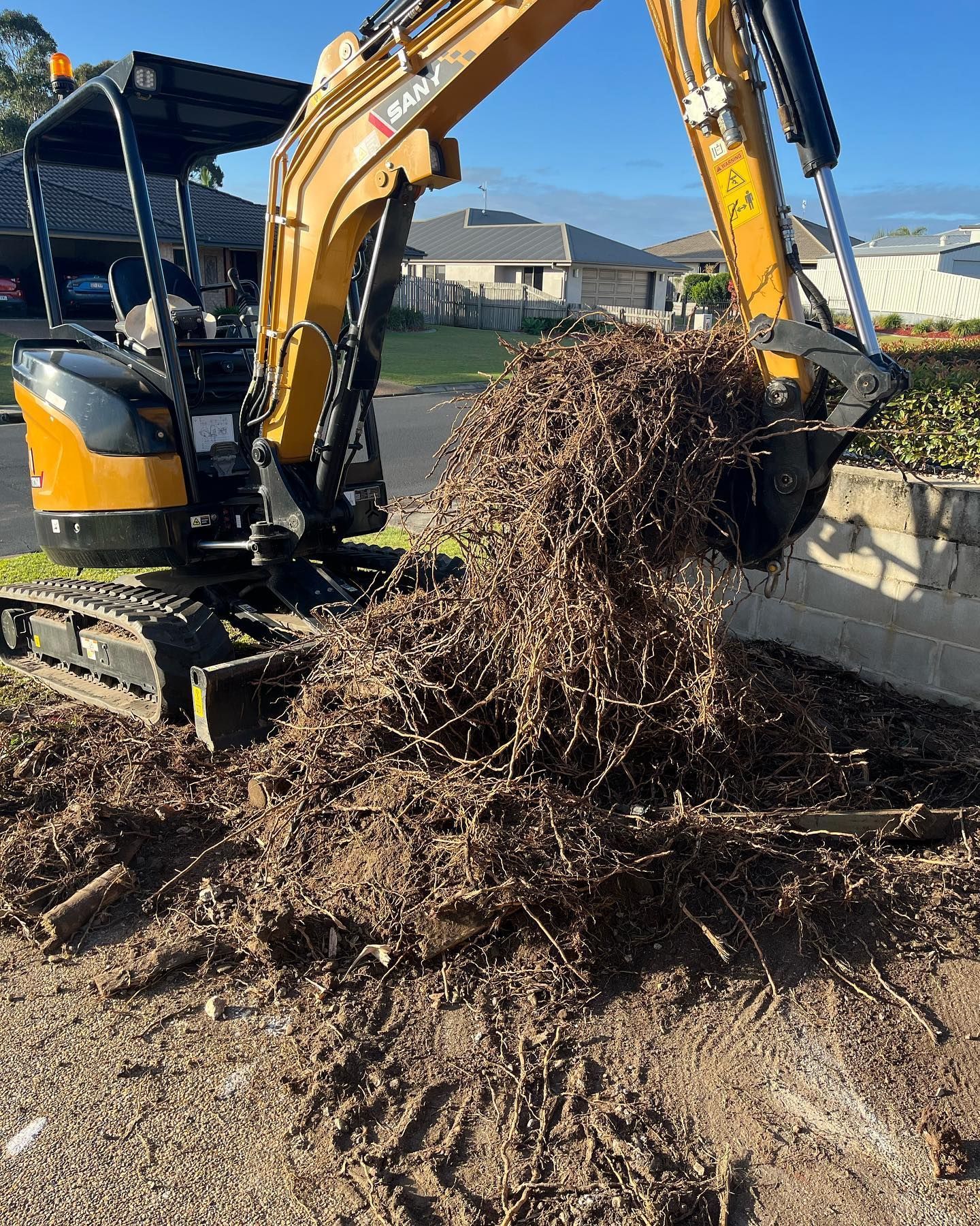 Yellow Excavator Dumping a Pile of Roots and Debris Onto the Ground — All Access Mini Earthworks in Innes Park, QLD
