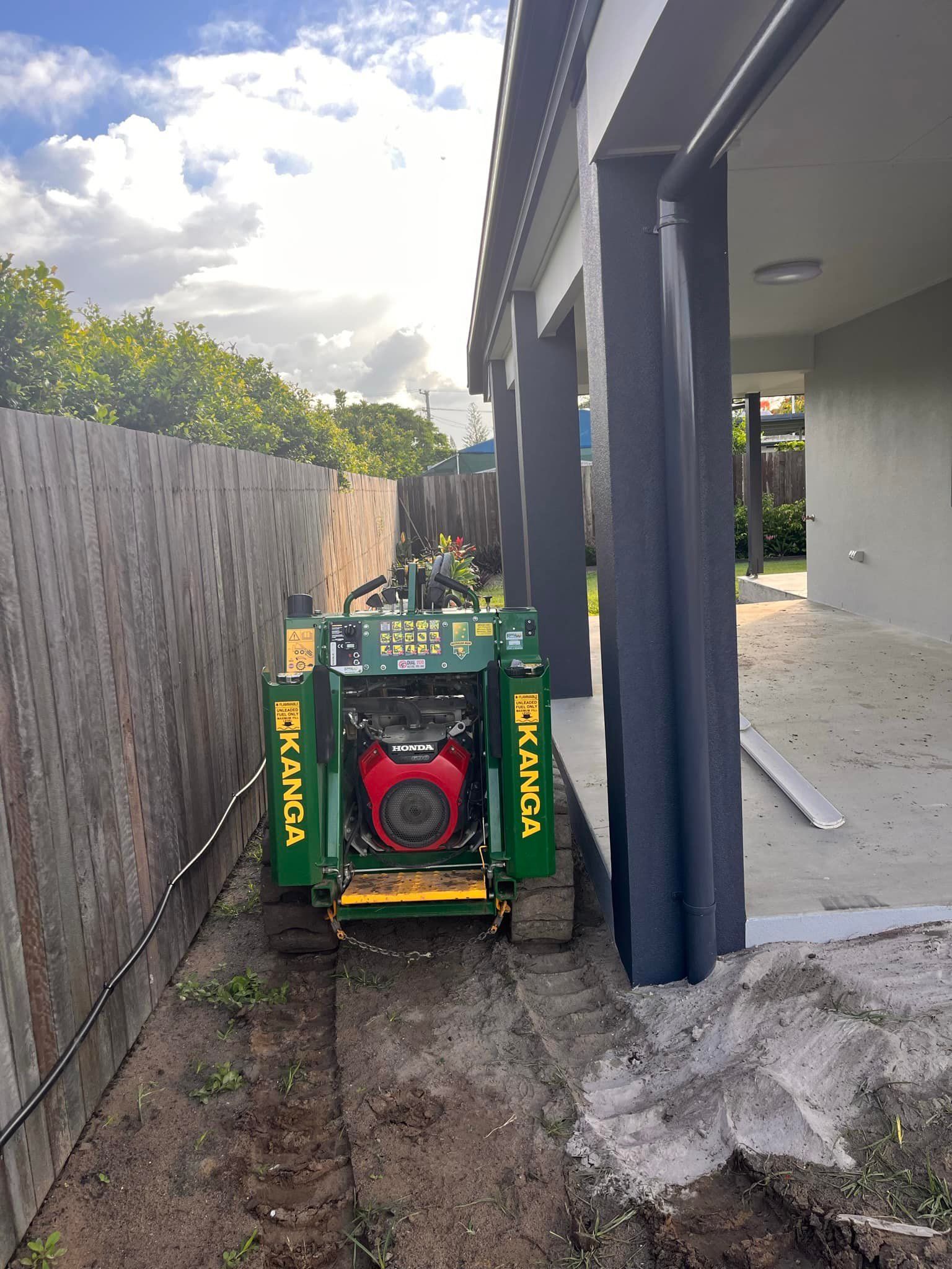 Green Trencher Digging Along a Wooden Fence Next to a House — All Access Mini Earthworks in Innes Park, QLD