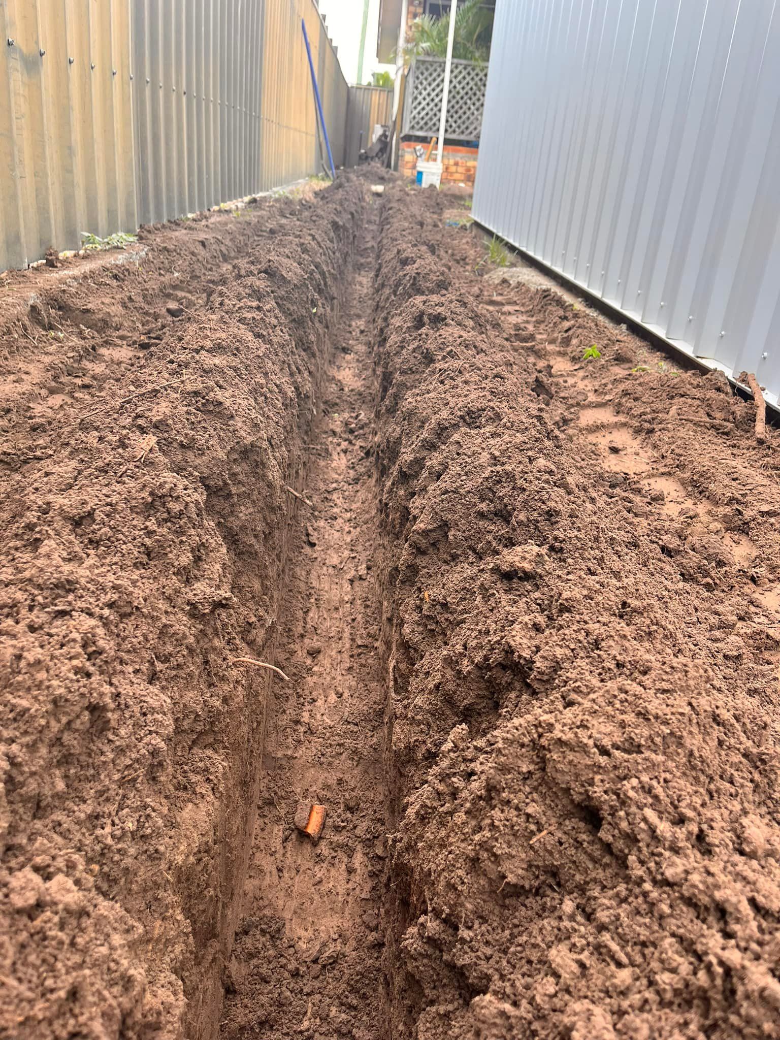 A Narrow, Dug Trench in Brown Soil Alongside a Corrugated Metal Fence — All Access Mini Earthworks in Gin Gin, QLD