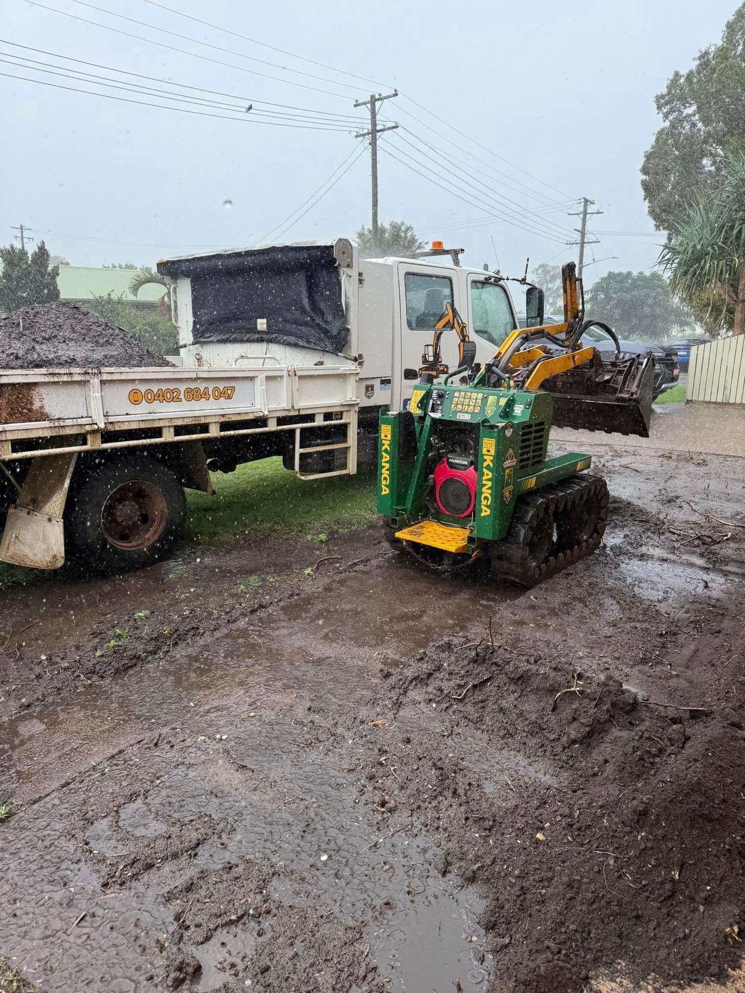Green and Yellow Mini-excavator on Muddy Ground Near a White Truck — All Access Mini Earthworks in Childers, QLD