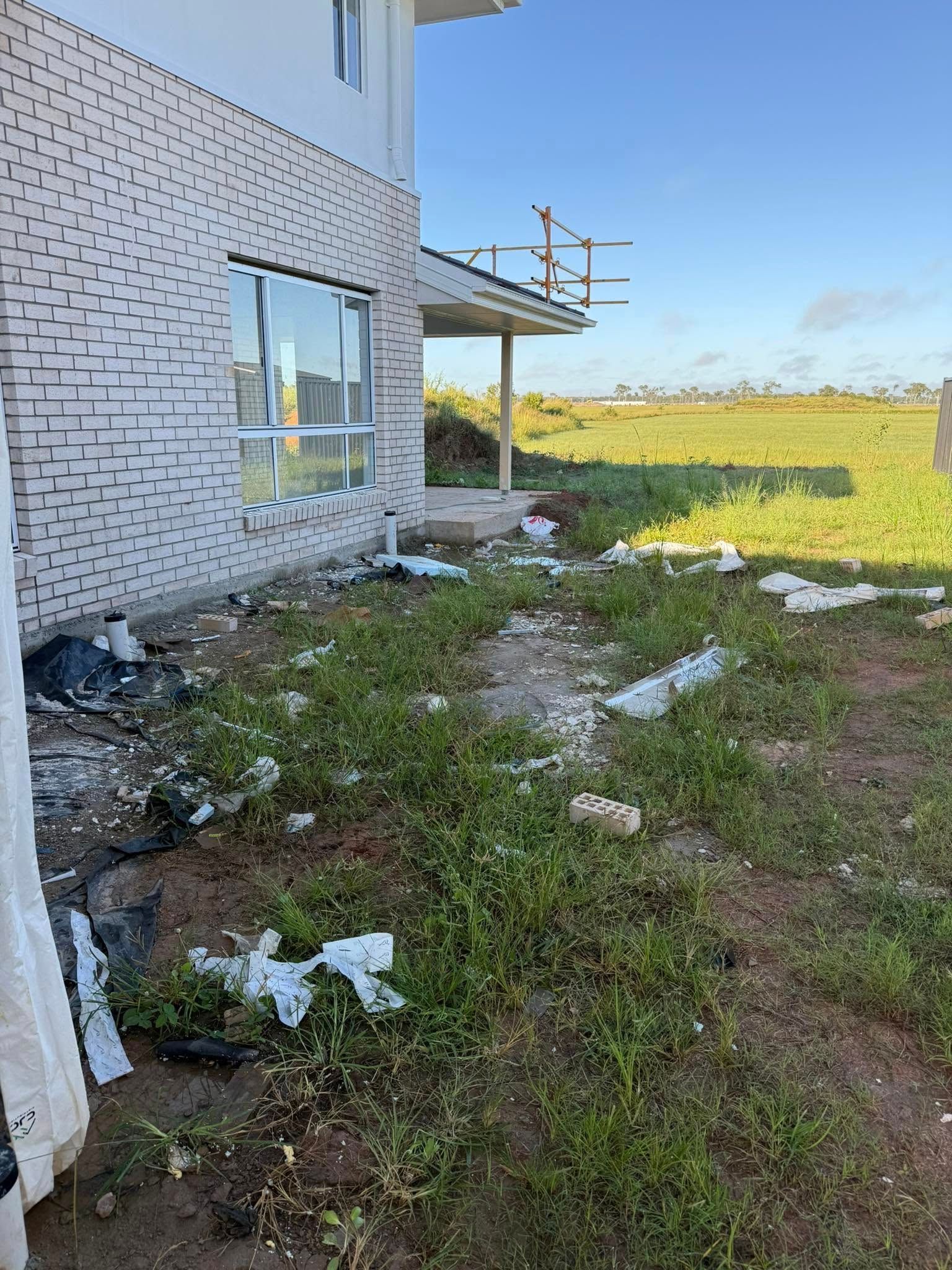 Side of a New Brick House With Overgrown Weeds and Construction Debris — All Access Mini Earthworks in Childers, QLD