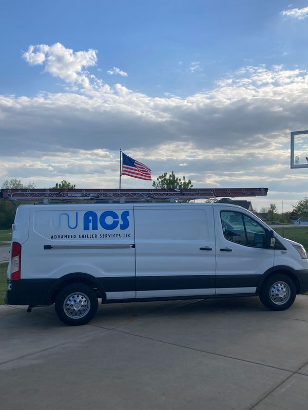White service van with TUNOS logo parked by water under a cloudy sky, with an American flag flying nearby