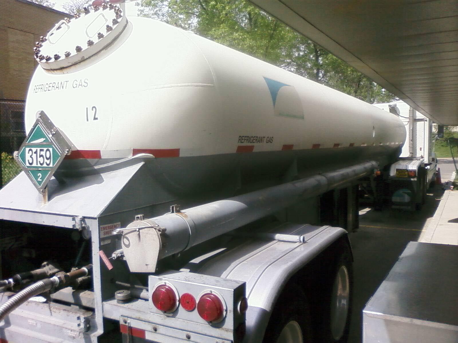 White tanker truck, potentially transporting hazardous material, under a canopy at a gas station.