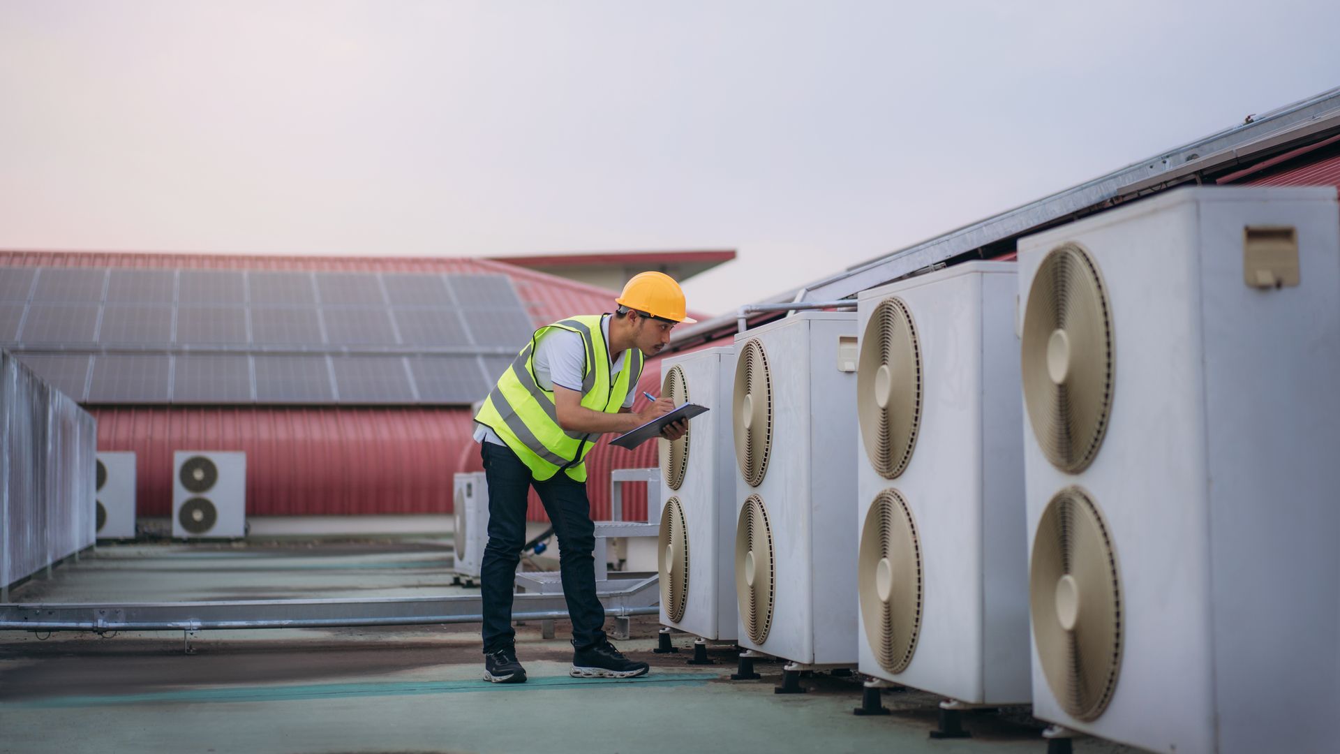 Worker in a hard hat inspects rooftop HVAC units on a flat industrial roof.