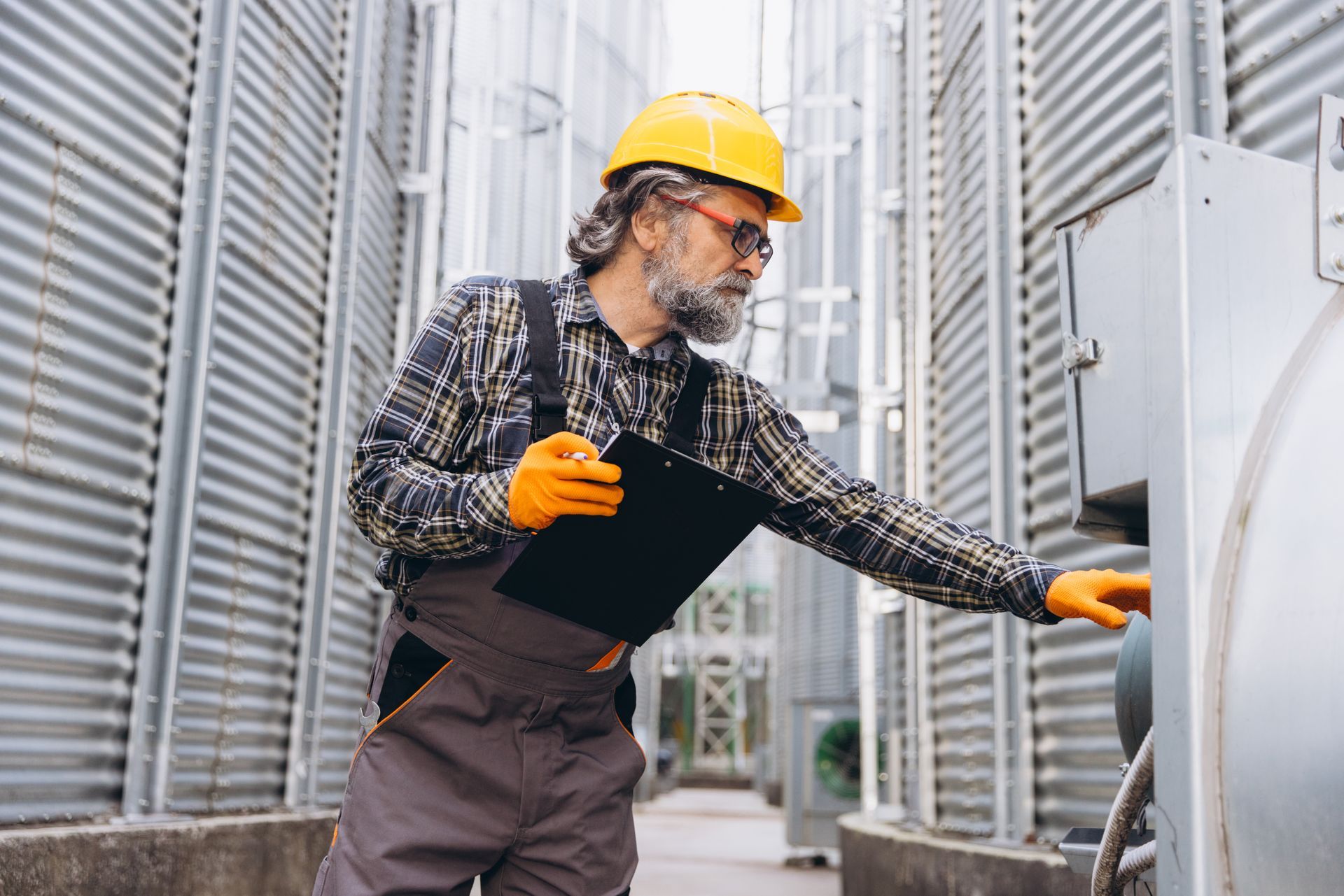 Worker in hard hat and gloves inspecting equipment in an industrial facility.
