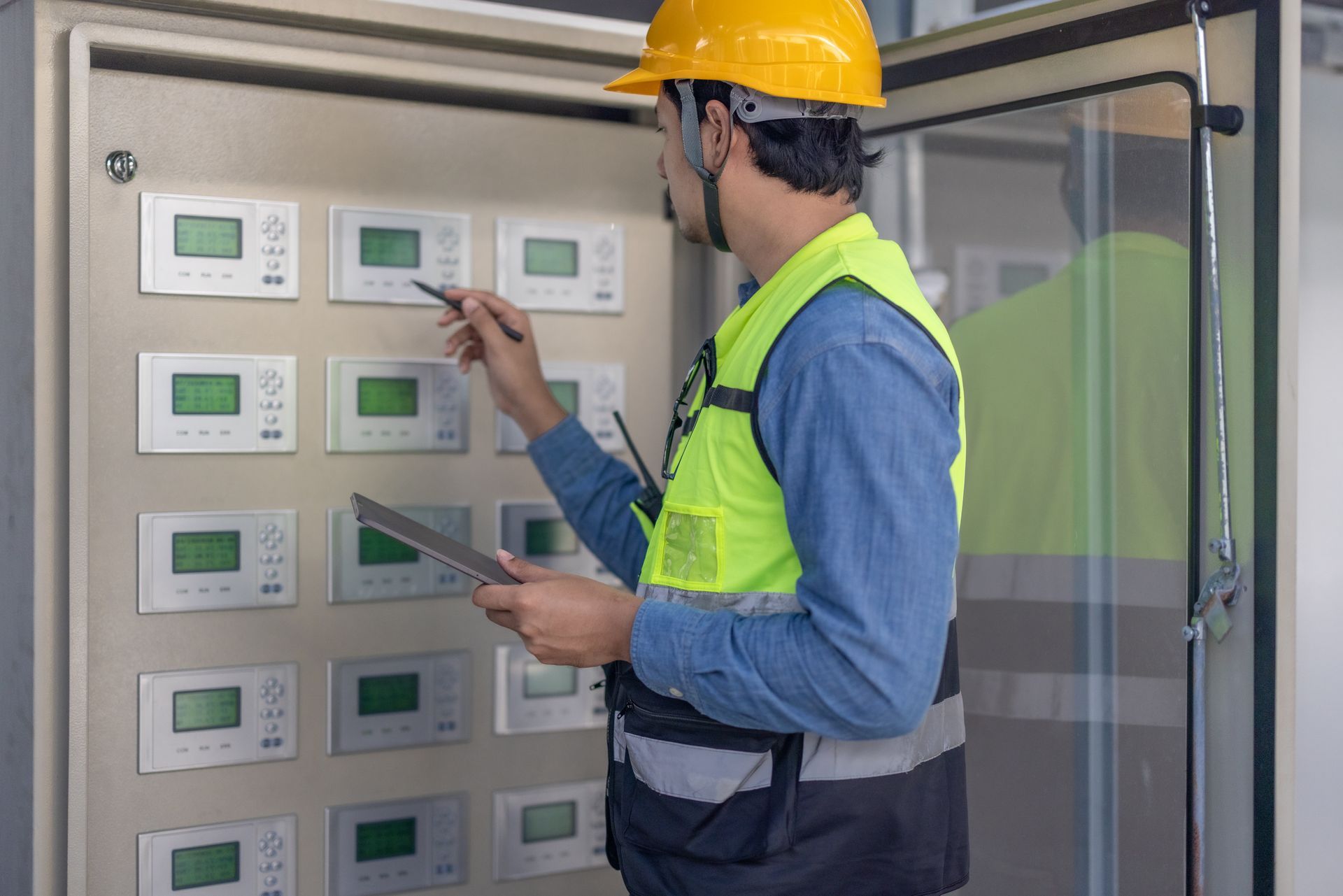 Worker in yellow hard hat inspecting electrical control panels in a utility room