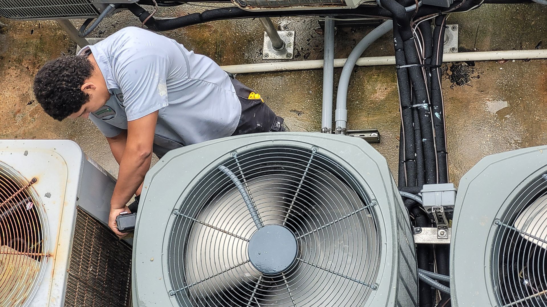 Technician inspecting rooftop HVAC units beside exposed piping and wiring
