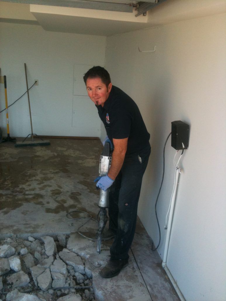 Person using a jackhammer to break concrete in an unfinished room