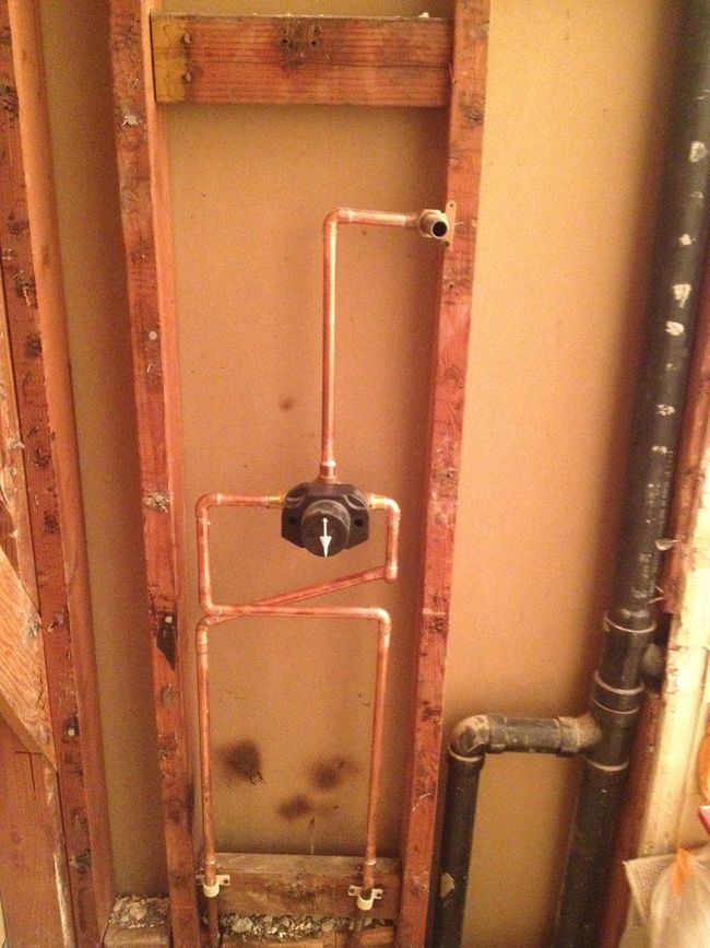 Exposed plumbing and copper pipework inside an unfinished wall with a black valve handle.