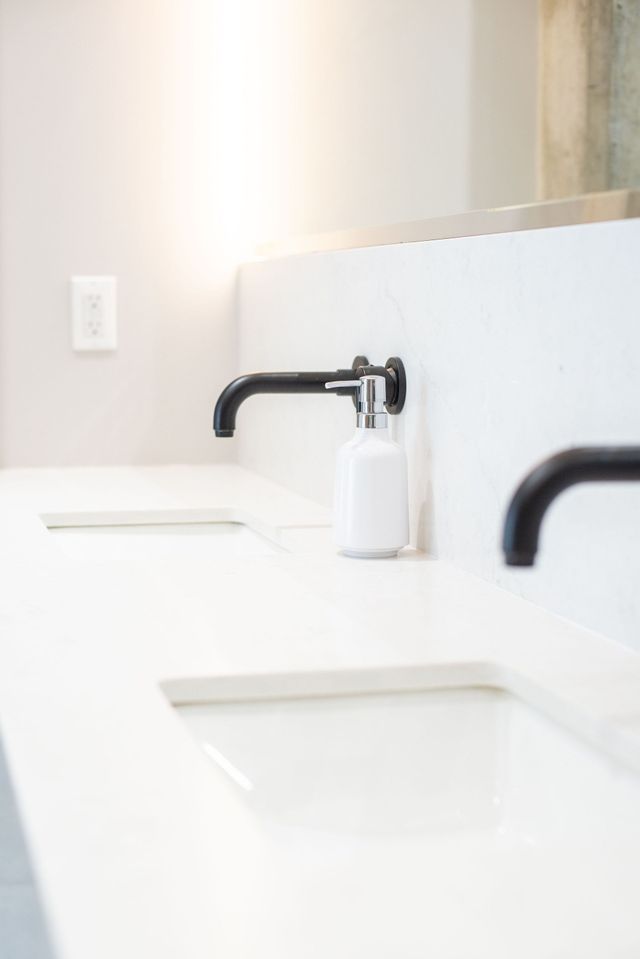 Modern white bathroom sink with black faucet and soap dispenser in front of a mirror