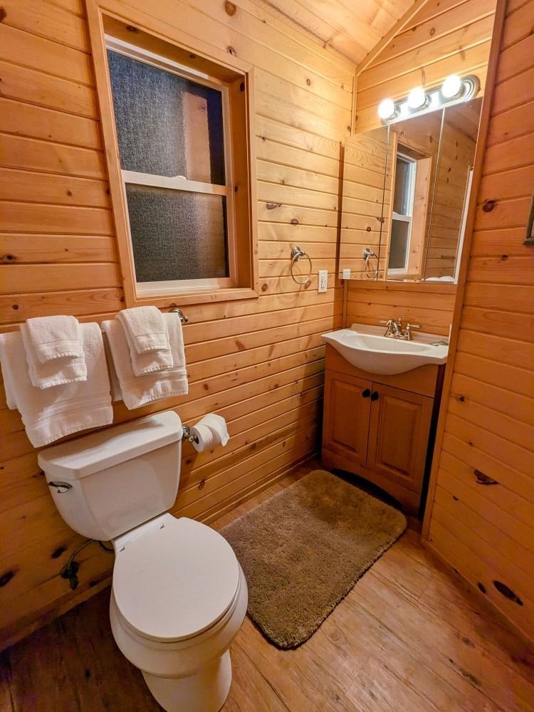 A bathroom with a toilet , sink , mirror and window.