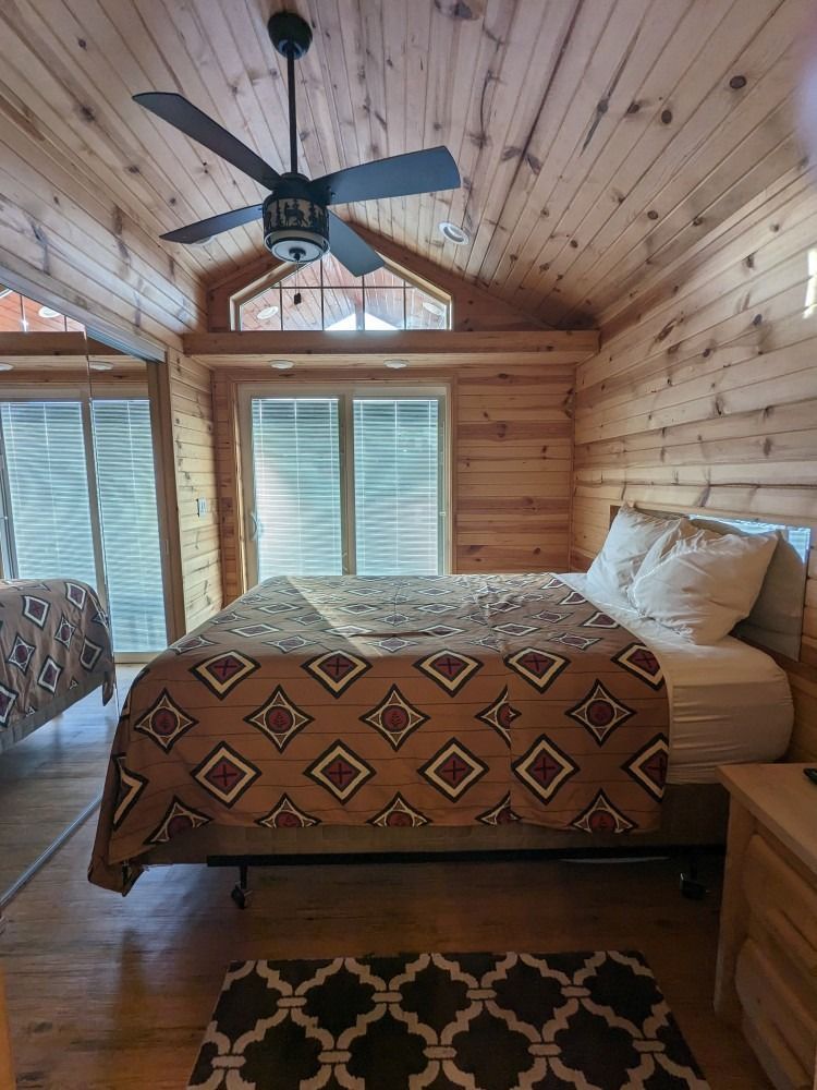 A bedroom in a log cabin with a bed and a ceiling fan.