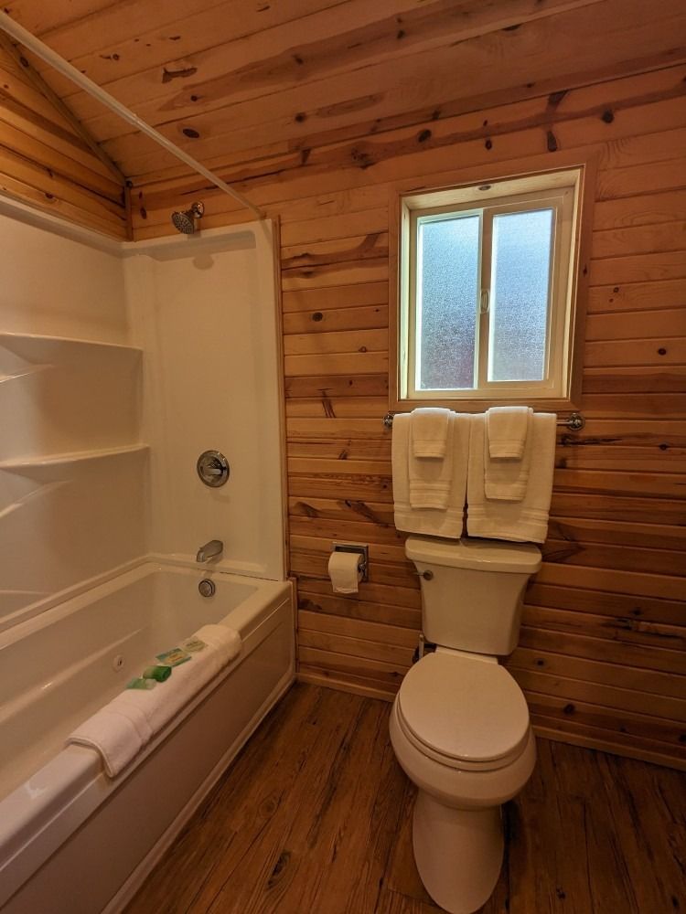 A bathroom with a toilet , tub , shower and window.