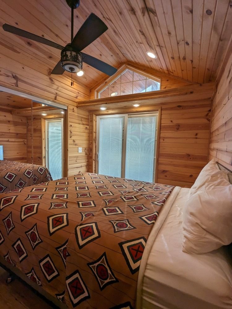 A bedroom in a log cabin with a ceiling fan and a bed.