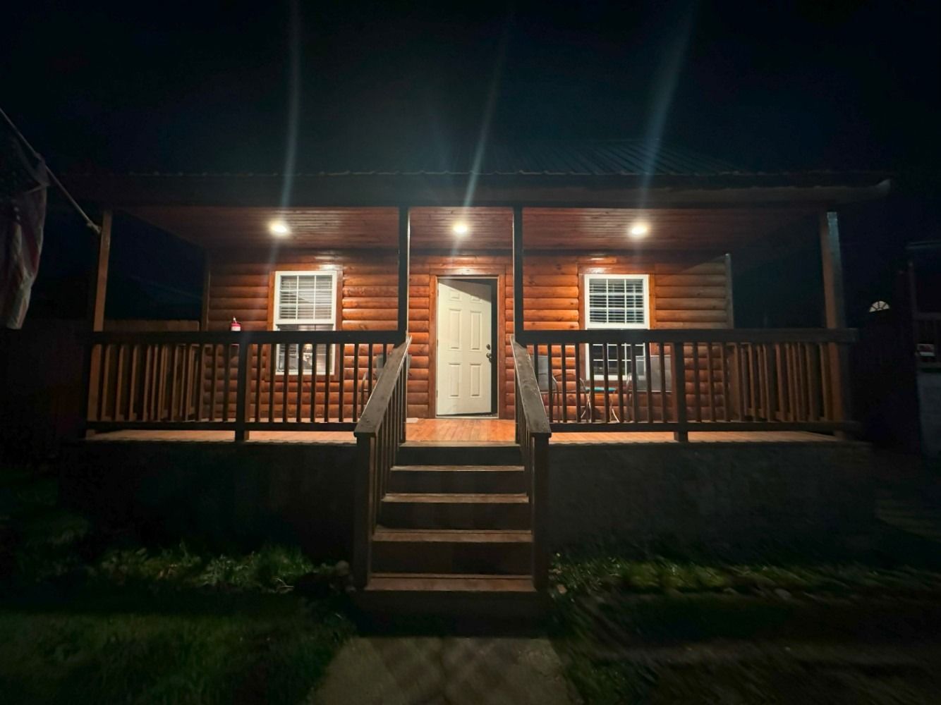 A small log cabin with a porch and stairs at night.