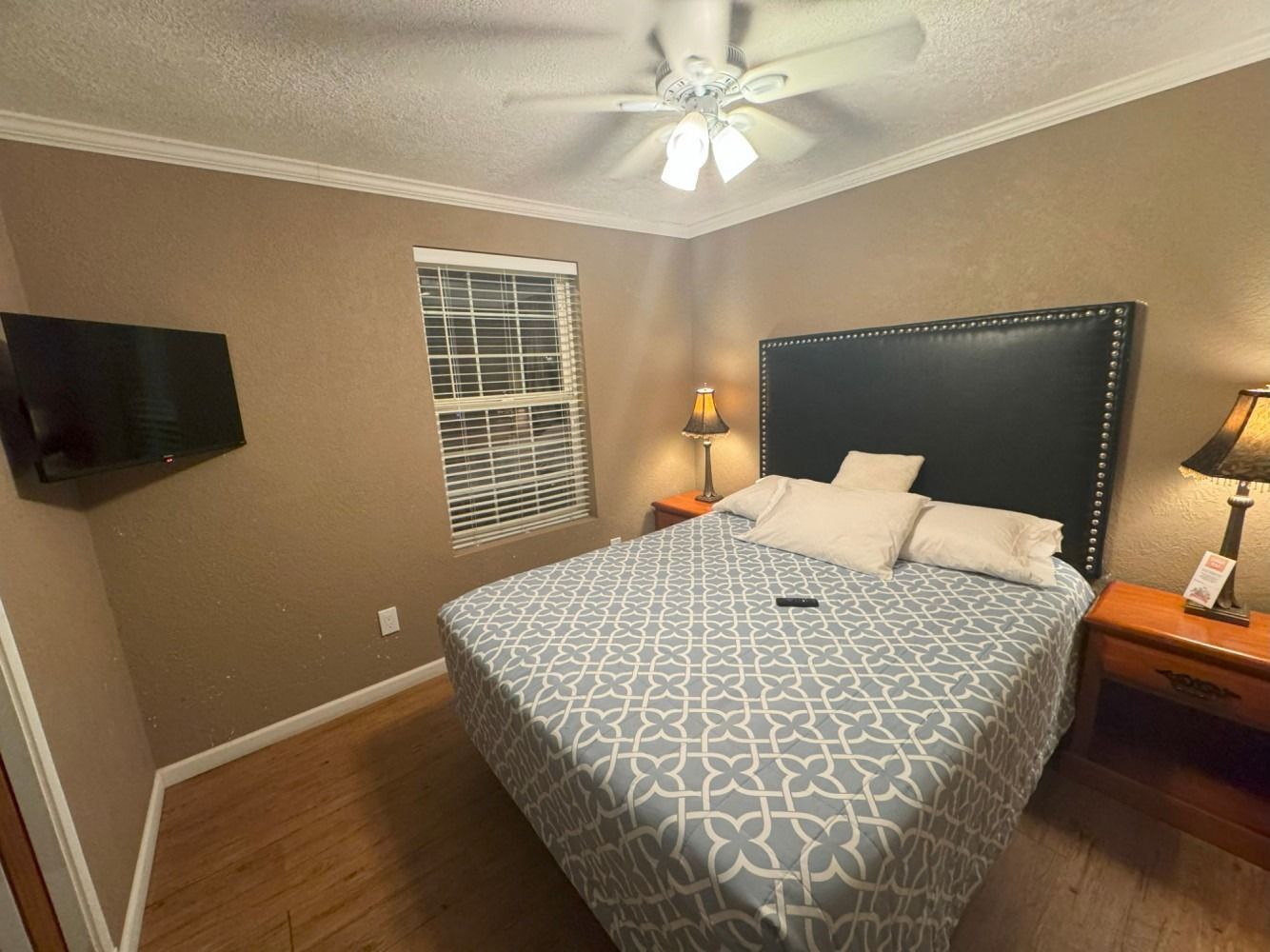 A bedroom with a bed , nightstand , television and ceiling fan.