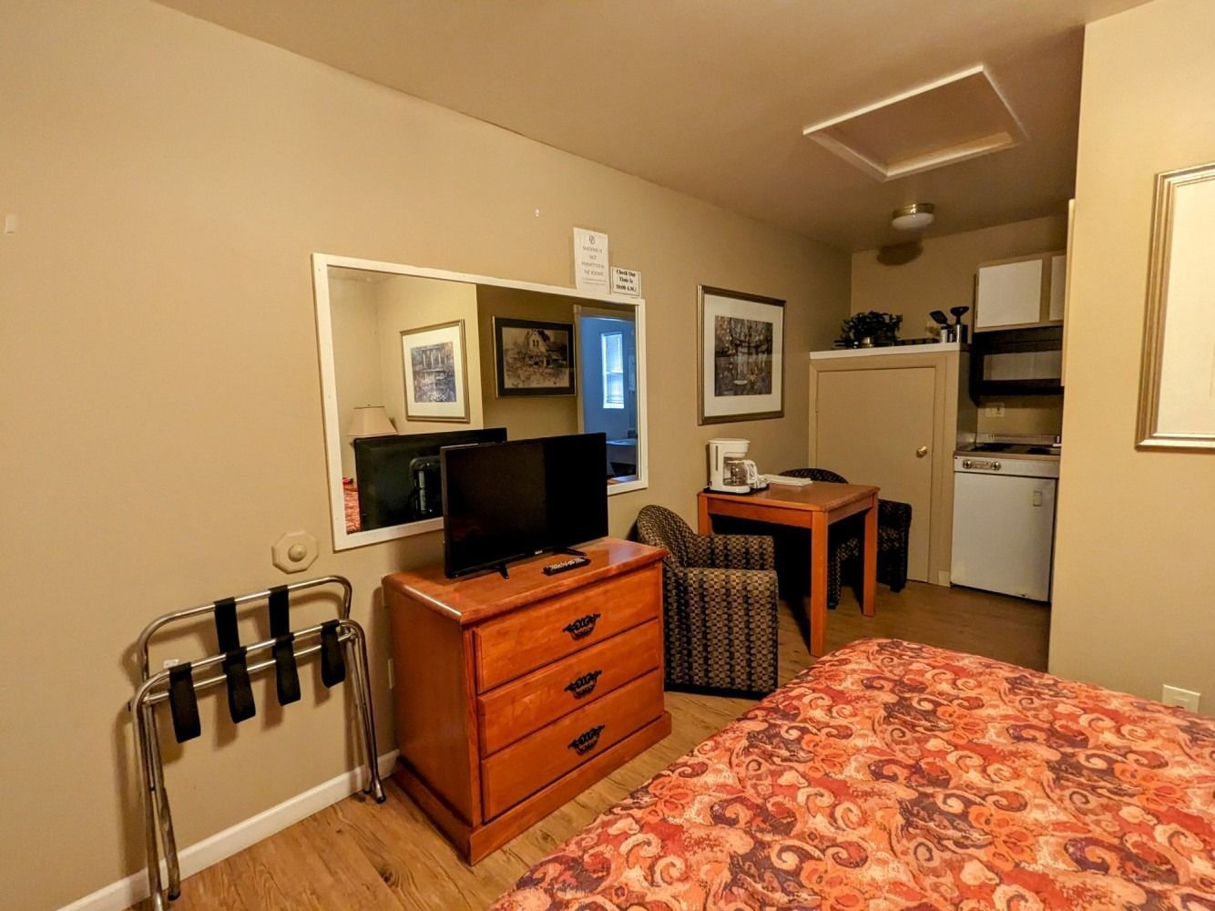 A hotel room with a bed , dresser , television and mirror.