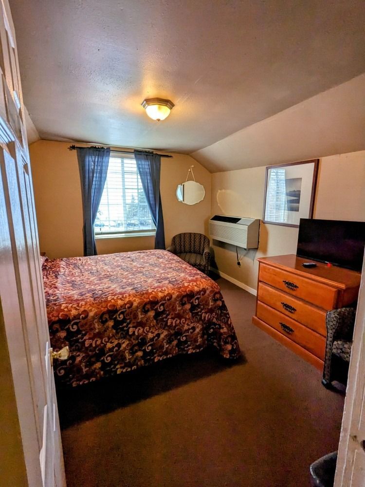 A bedroom with a bed , dresser , chair and television.