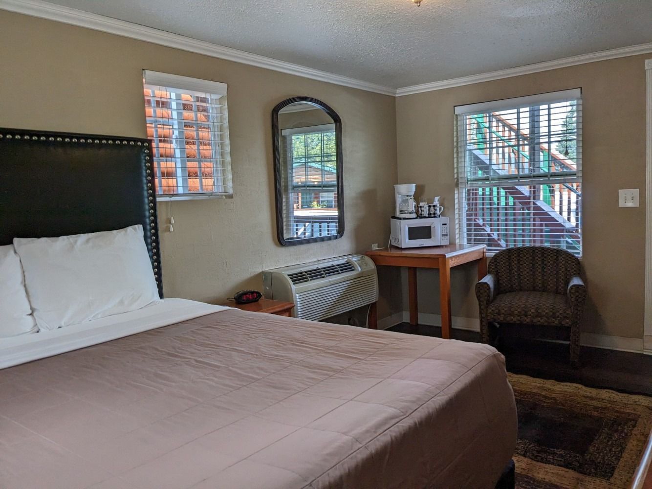 A hotel room with a bed , chair , table , microwave and mirror.
