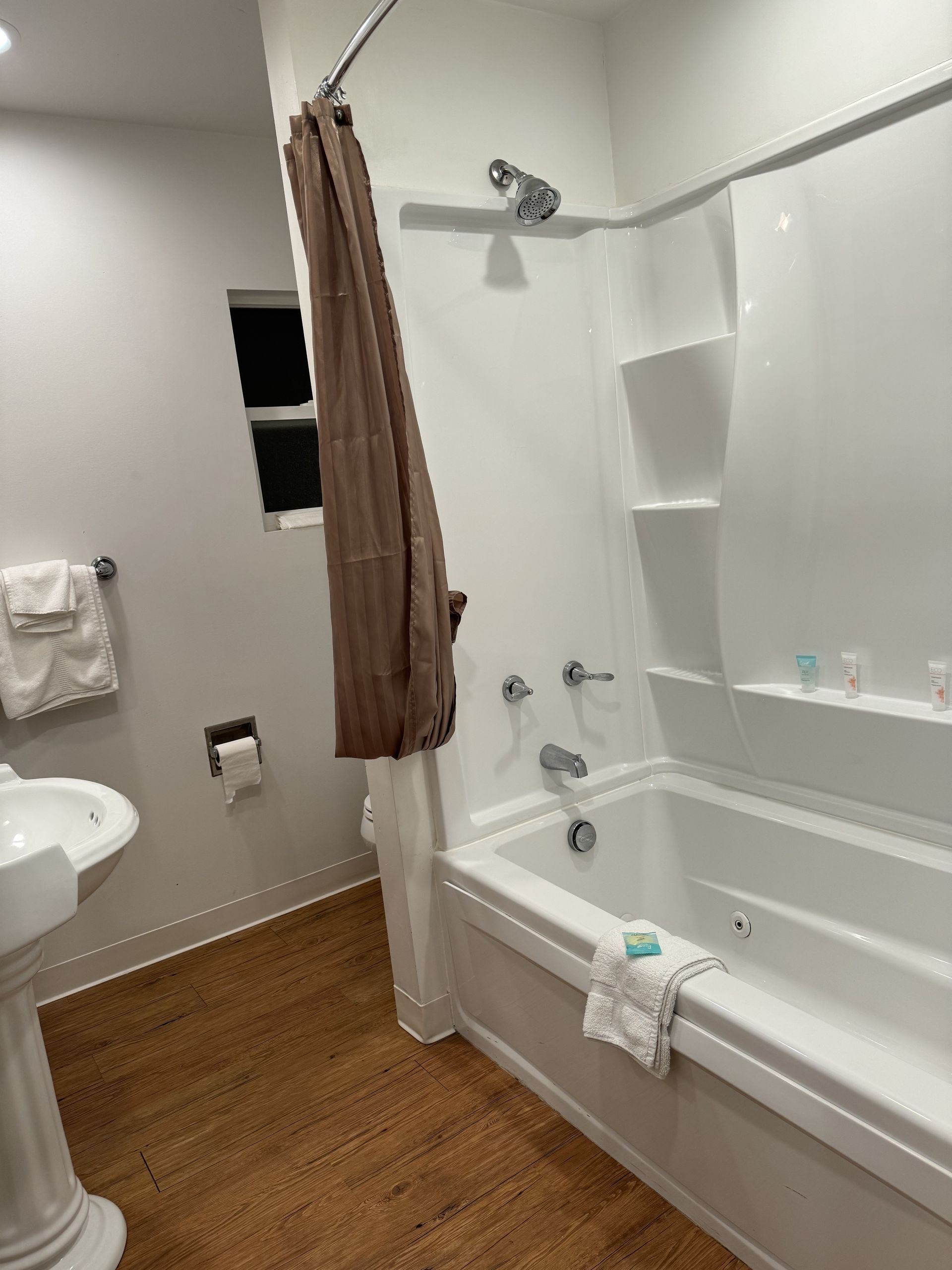 A bathroom with a tub , sink , shower and window.