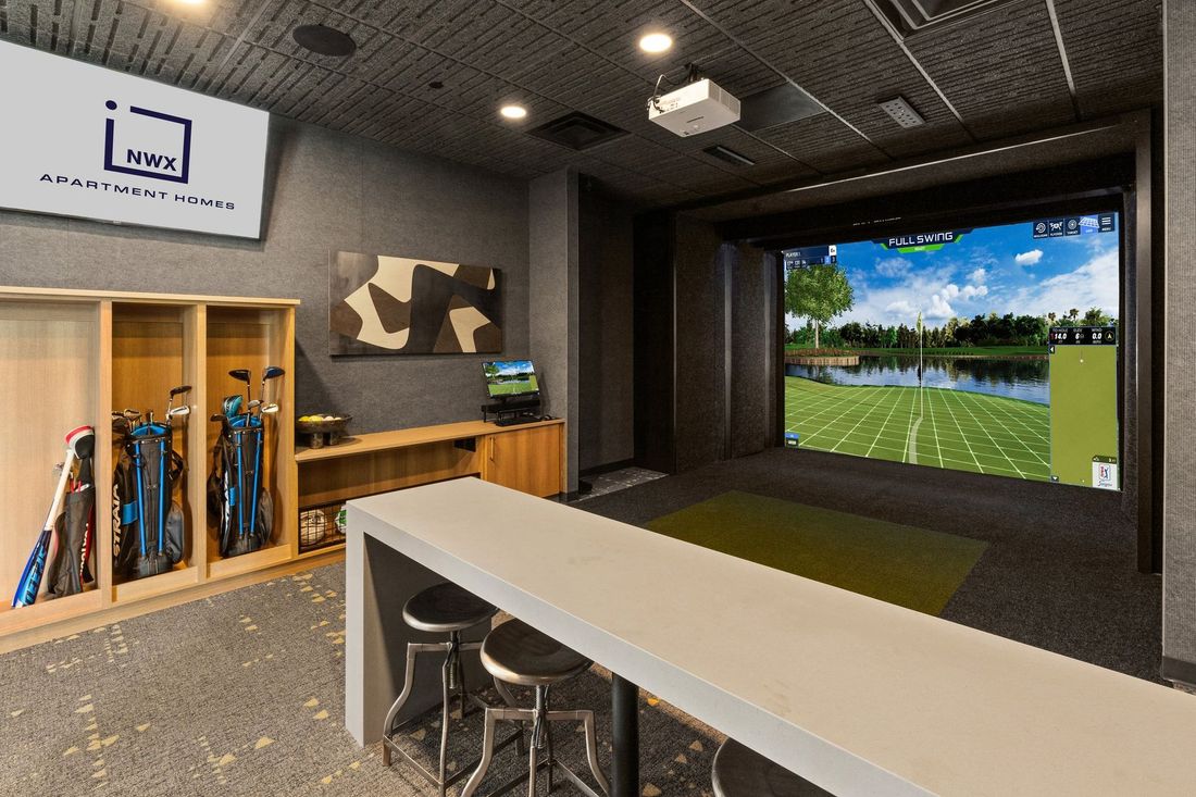 Golf simulator room with a screen, golf clubs, and a bar area.