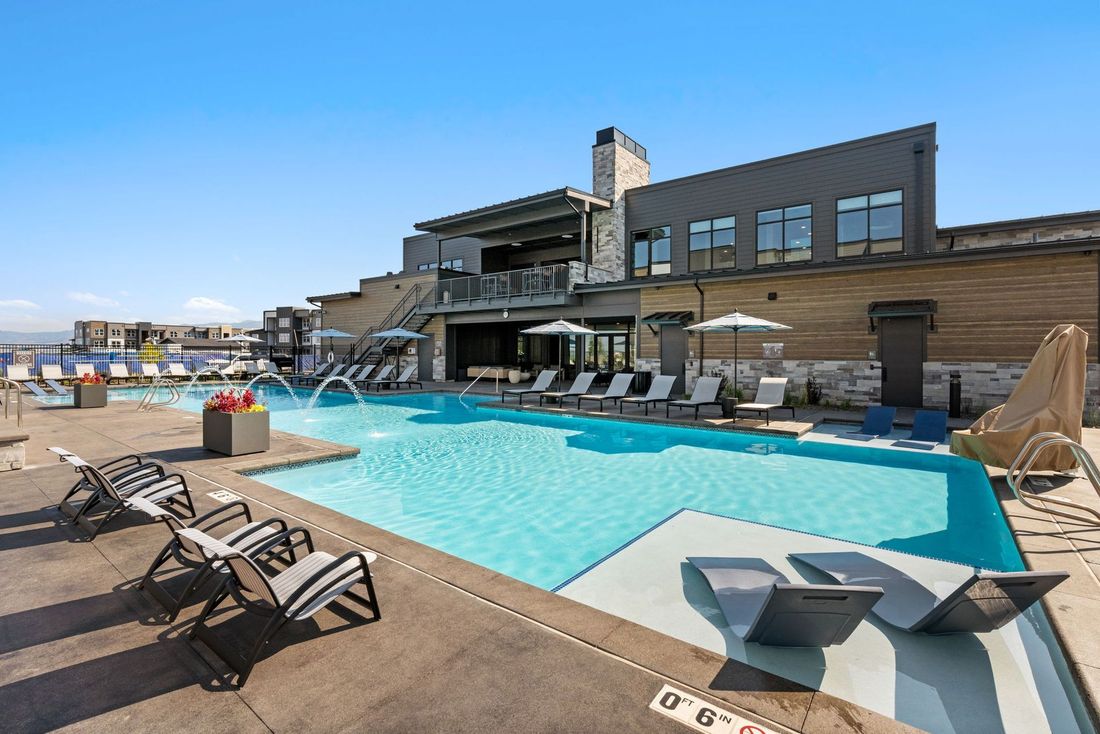 Pool with lounge chairs and water fountains, next to a modern building under a blue sky.