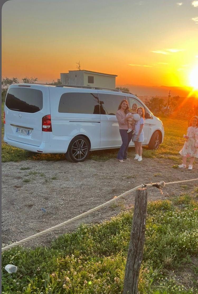 Furgone bianco con persone in posa accanto, tramonto sullo sfondo.