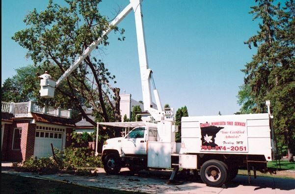 Utility truck with bucket lift working near a house and trees on a sunny day