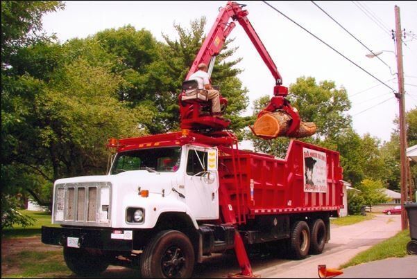 Red utility truck with raised crane arm lifting equipment beside a roadside.