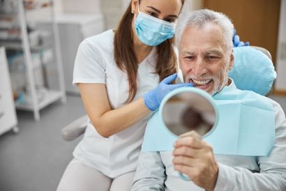 Dentist showing older patient his teeth in a mirror.
