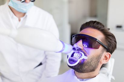 Man having teeth whitened at the dentist; blue light shines on his teeth.